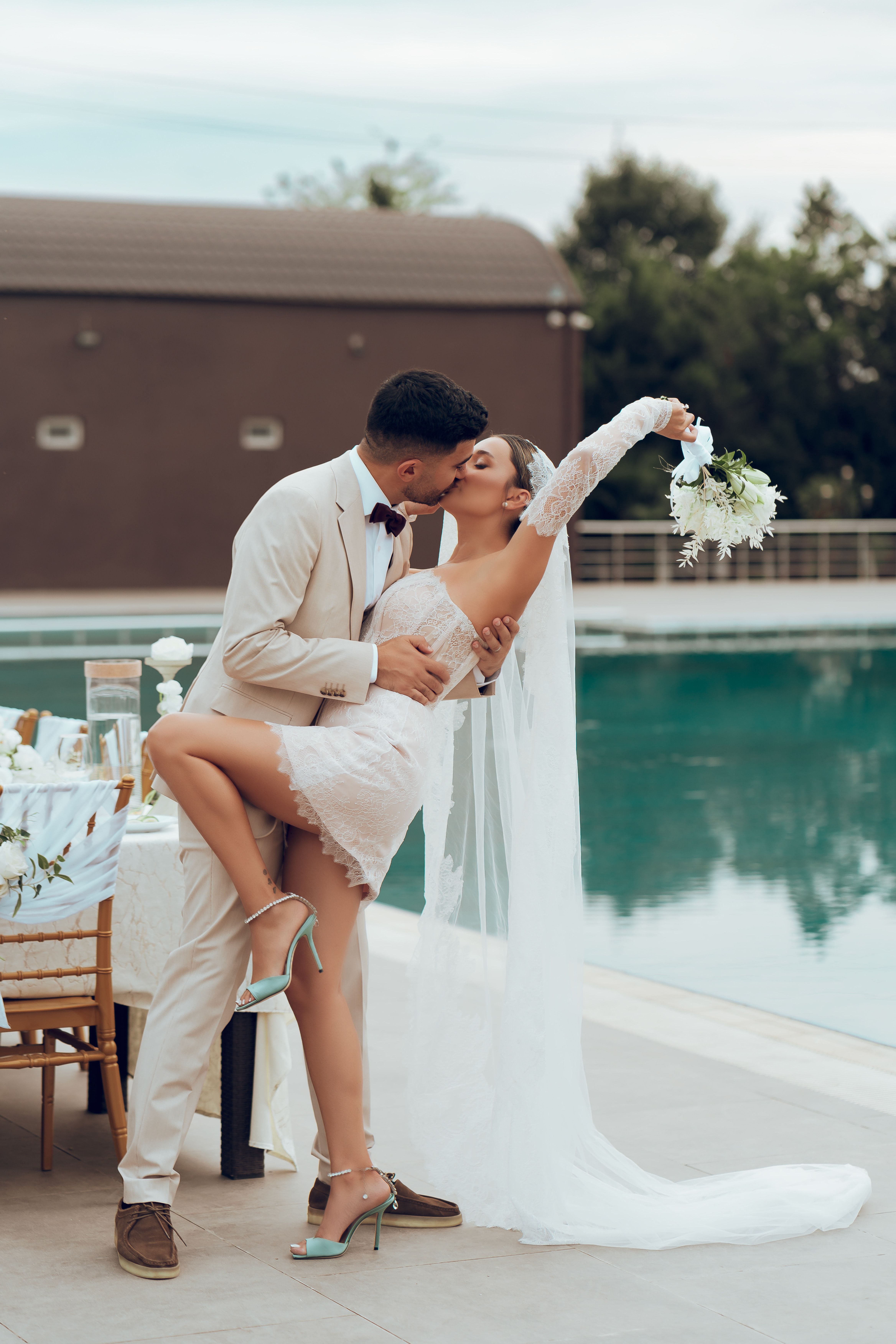 Newlywed couple sharing a kiss beside a pool at an outdoor wedding celebration