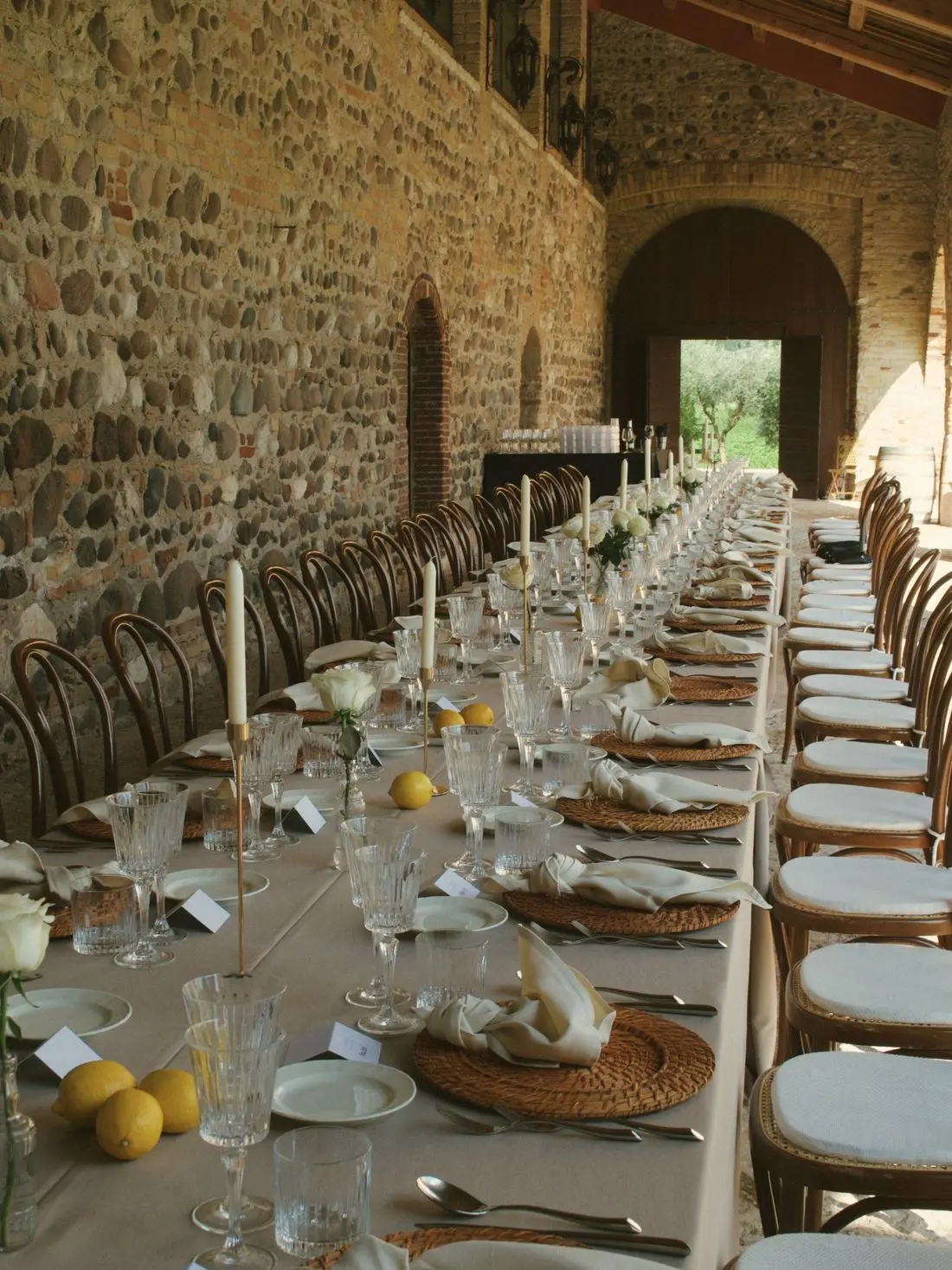 One long table laid down a vaulted stone hall, lemons and rattan on cream linen