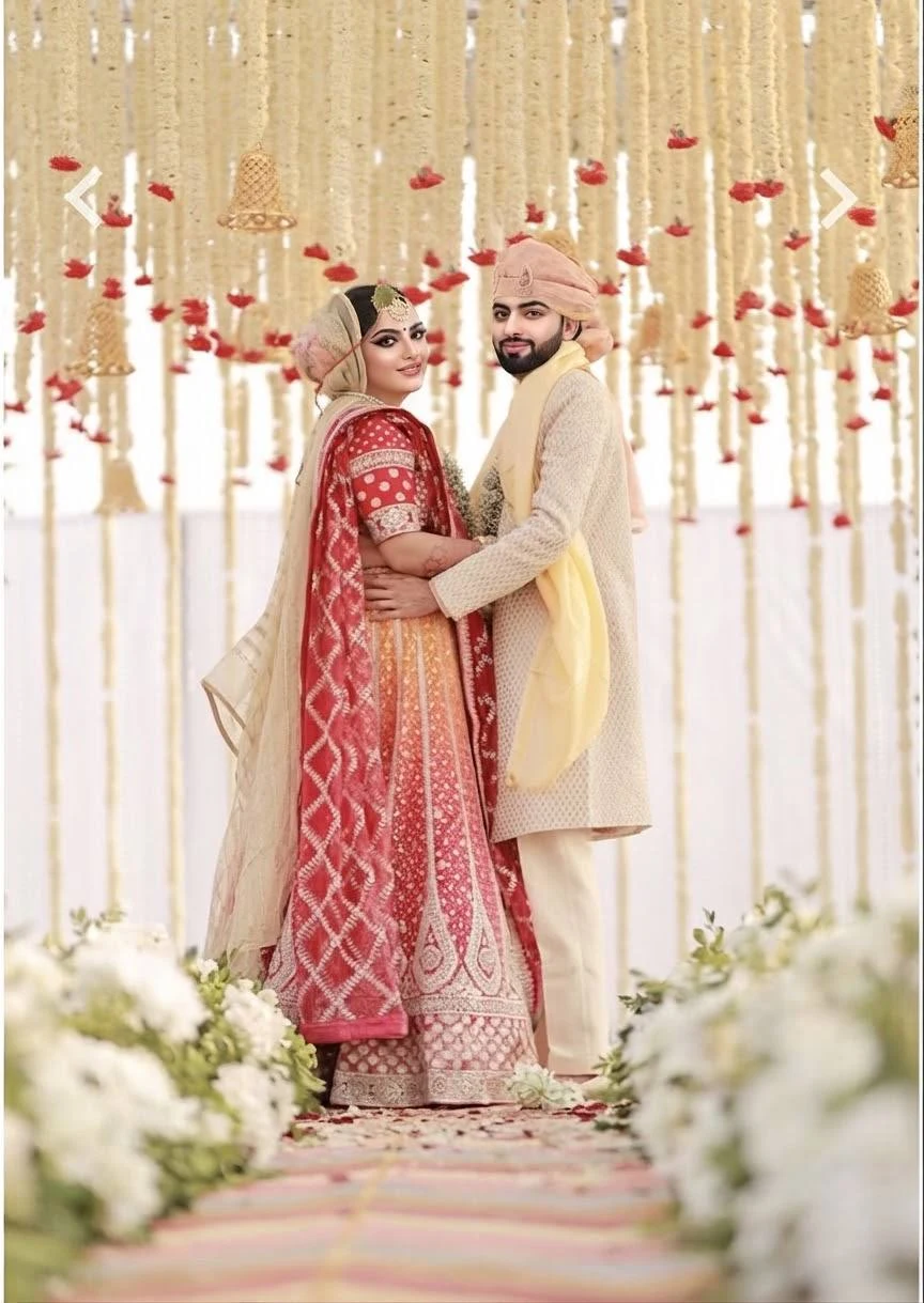Indian wedding couple in traditional red and ivory wedding attire beneath floral decorations